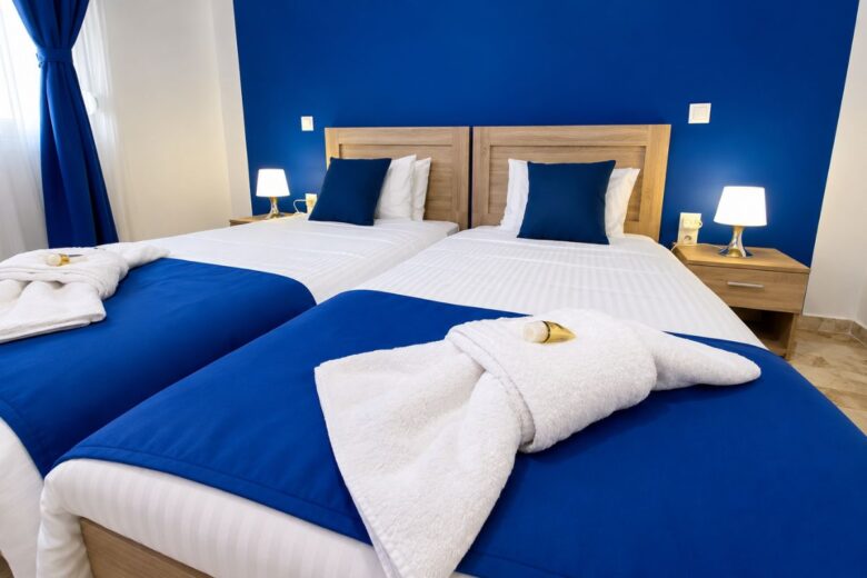 Κομψό υπνοδωμάτιο στο Patras Blue Suite με δύο άνετα μονά κρεβάτια, λευκά είδη υψηλής ποιότητας, μπλε διακόσμηση και ατμοσφαιρικό φωτισμό