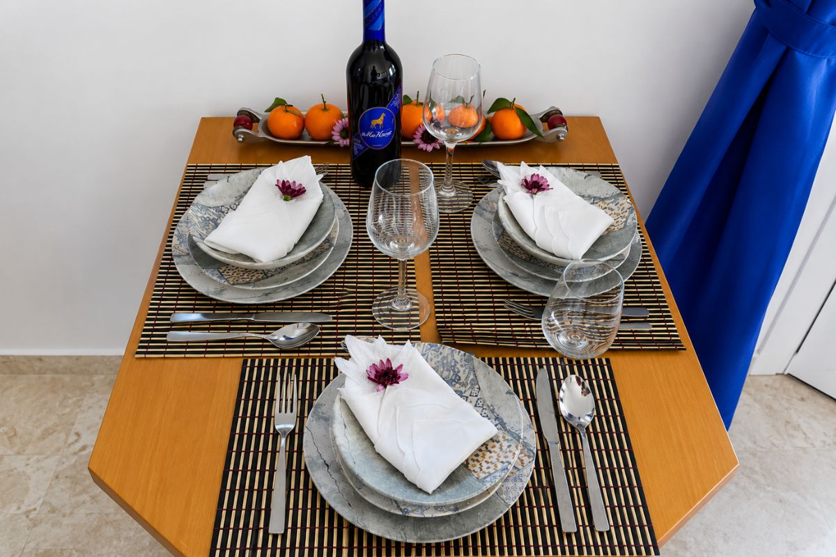 Καλαίσθητη τραπεζαρία στο Patras Blue Suite με σερβίτσιο για τρία άτομα, ποτήρια κρασιού, διακοσμητικά λουλούδια και κρασί καλωσορίσματος