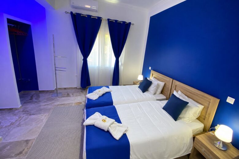 Φωτεινό υπνοδωμάτιο στο Patras Blue Suite με δύο άνετα μονά κρεβάτια, κλιματισμό, κομοδίνα και μοντέρνα διακόσμηση σε μπλε αποχρώσεις