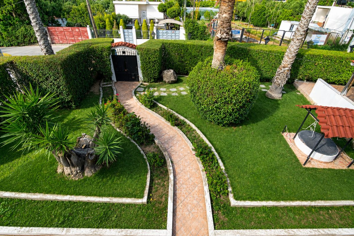 Περιποιημένος ιδιωτικός κήπος στο Patras White Castle με καταπράσινο γκαζόν, φοίνικες, πλακόστρωτα μονοπάτια και καθιστικό εξωτερικού χώρου